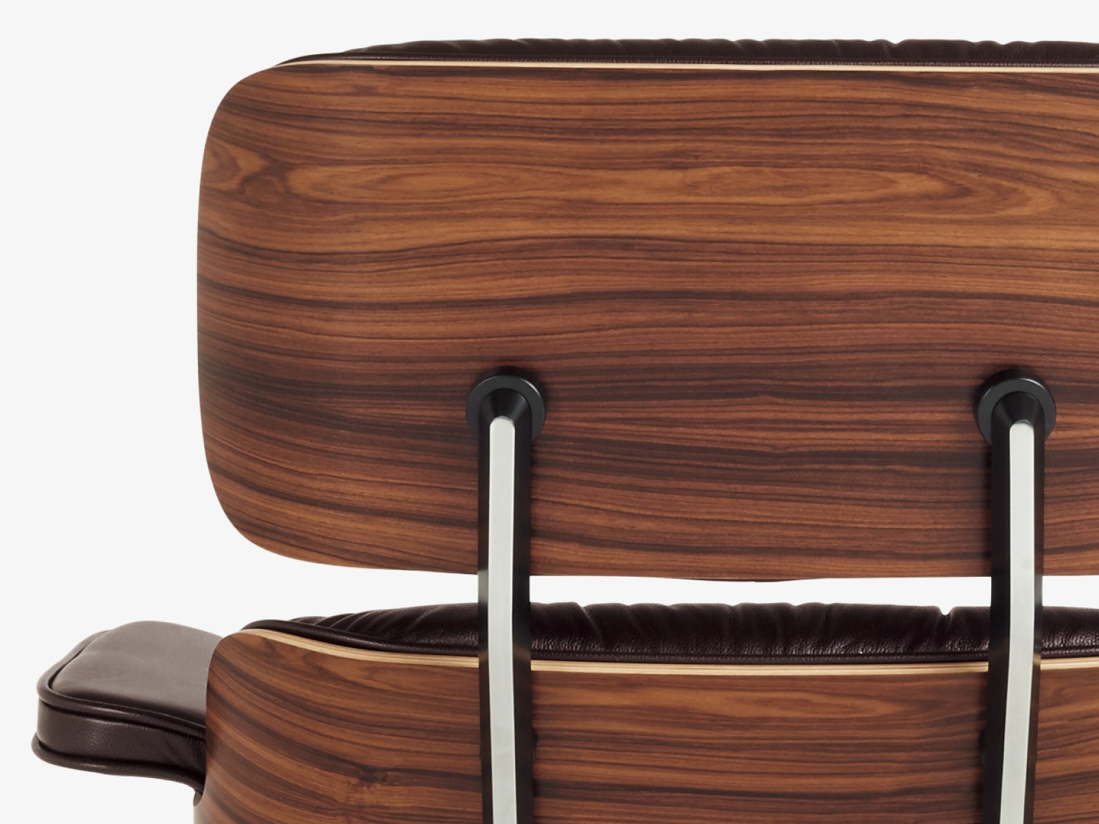 Close-up of the back of an Eames Lounge Chair with a wood veneer shell and black leather. 